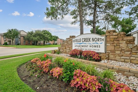 A sign for Estelle Creek North Apartment Homes sits in front of a flower bed in Irving, TX